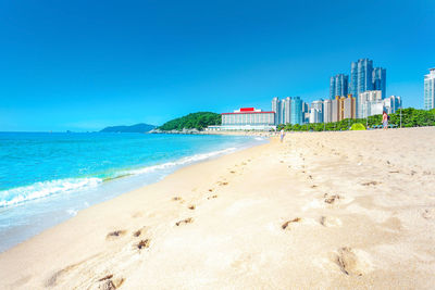 Scenic view of beach by buildings against clear blue sky