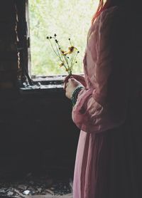 Midsection of woman standing with flowers in abandoned home