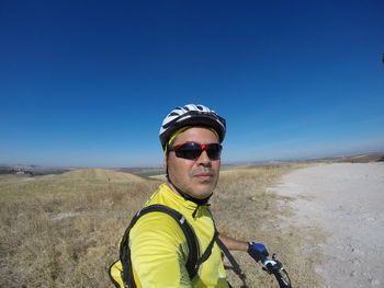 Side view portrait of man riding bicycle on field against blue sky