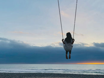 Rear view of girl swinging at beach during sunset