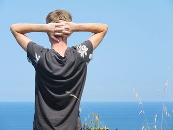 Rear view of teenage boy standing against sea