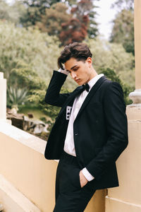 A beautiful young man, the groom in an elegant wedding suit, stands posing in the city's old park