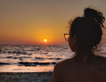 Side view of young woman at beach against sky during sunset