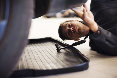 Close-up of technician repairing car while lying down in shop