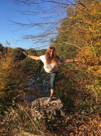 Full length of smiling woman balancing on tree stump in forest