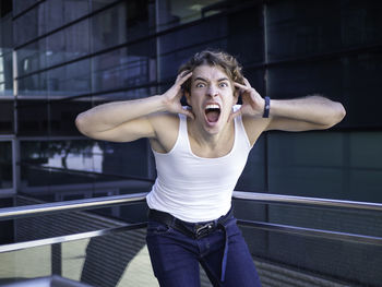 Young aggressive man in casual clothes screaming with hands on head looking at camera