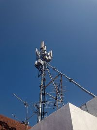 Low angle view of communications tower against building against clear blue sky