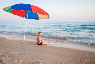 Woman sitting on beach by sea against sky