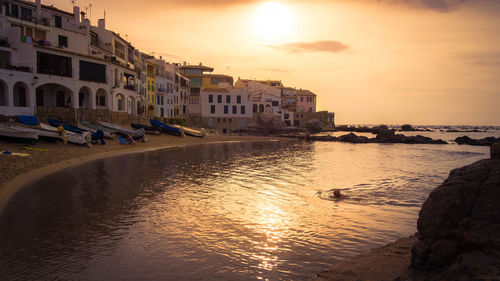 Buildings by sea against sky during sunset