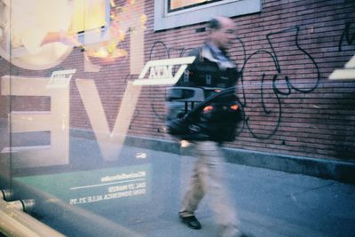 Man walking in street against building seen from glass