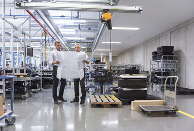 Two businessmen in factory hall discussing construction plan