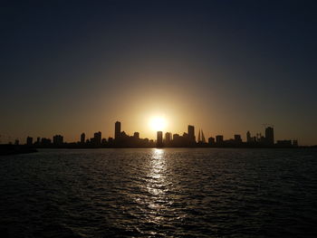 Silhouette buildings by sea against sky during sunset