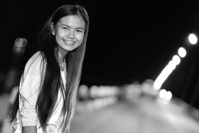 Portrait of happy young woman standing on footpath at night