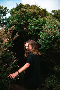 Side view of young woman standing against plants