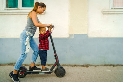 Woman and boy riding electric push scooter on street