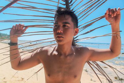 Young man with arms raised standing against sky