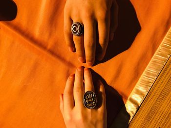 Close-up of man holding hands against orange wall