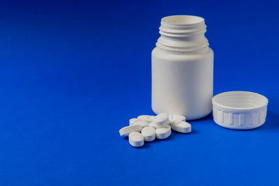 Close-up of pills spilling from bottle against blue background