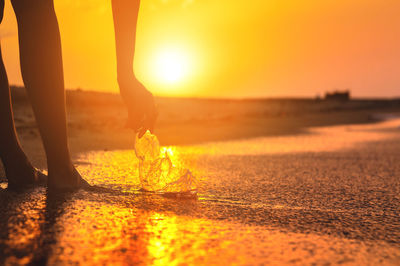 Low section of people walking on road during sunset