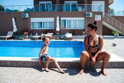 Full length of young woman with son sitting at poolside