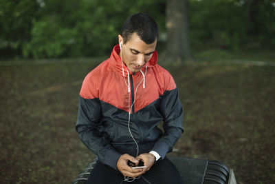 Man sitting on bench listening music at park