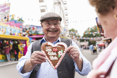 Portrait of happy senior man presenting gingerbread heart on fair