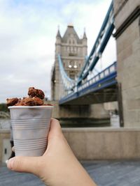 Midsection of person holding ice cream against bridge