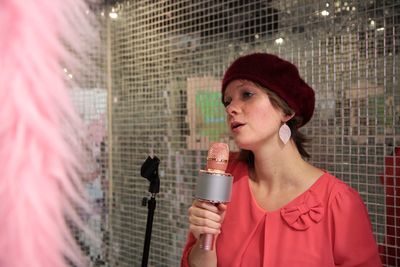 Young woman singing while holding microphone against net
