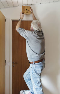 Senior man hanging wall clock above door at home
