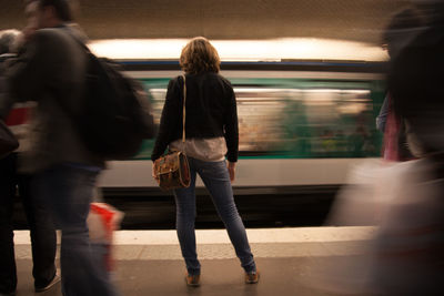 Rear view of woman standing at subway station against moving train during rush hour