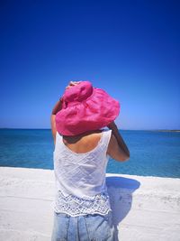 Woman wearing hat while standing on beach against clear blue sky