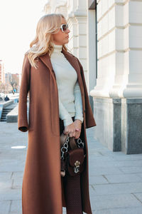 Young woman wearing long coat standing on sidewalk