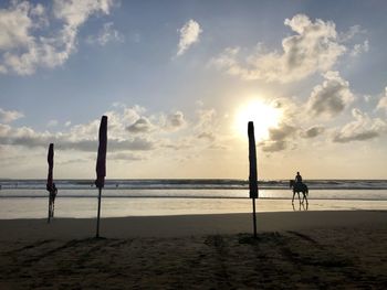 Silhouette wooden post on beach against sky during sunset