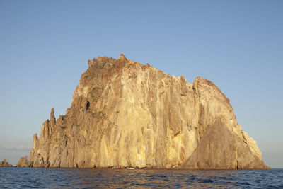 Rock formations by sea against clear blue sky
