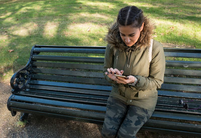 High angle view of woman using smart phone while sitting on bench at park