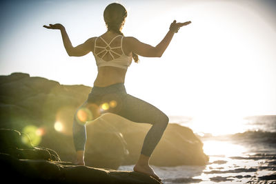 Full length of woman exercising on rock against sea