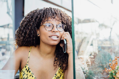 African american female with curly hair sitting in cafe and speaking on mobile phone while relaxing and looking away