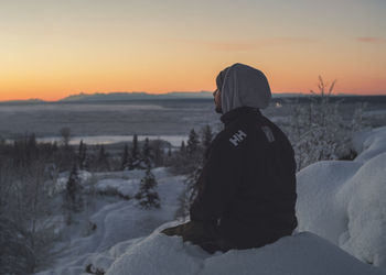 Rear view of man standing on snow covered land during sunset