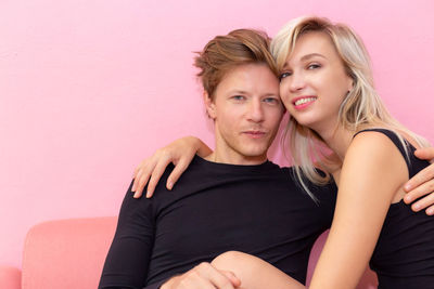 Portrait of young couple sitting against pink wall