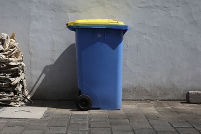 Garbage can on sidewalk against wall