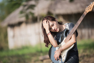 Portrait of young woman holding electric guitar while sitting on audio equipment