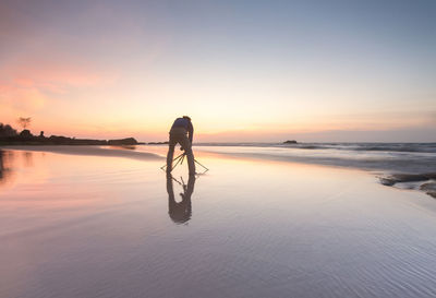 Silhouette person in sea against sky during sunset