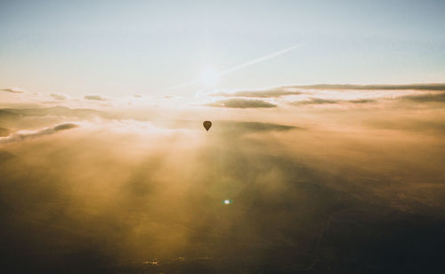 Hot air balloon flying over foggy landscape against sky during sunrise