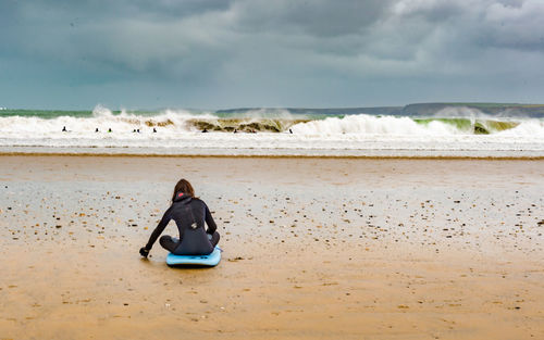 Rear view of woman sitting on surfboard at beach