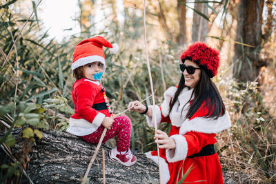 Cute baby girl with mother wearing santa costume in forest