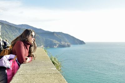 Woman looking at sea by mountain against sky