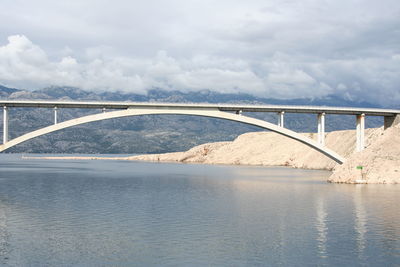 Arch bridge over sea against cloudy sky