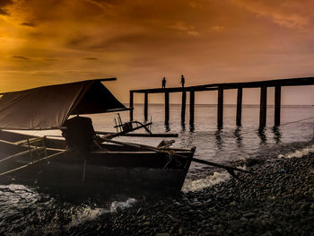 Silhouette boat moored on beach against sky during sunset