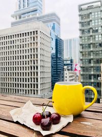 Close-up of cherries by yellow mug on table against cityscape