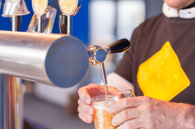 Cropped hands pouring beer from tap in glass